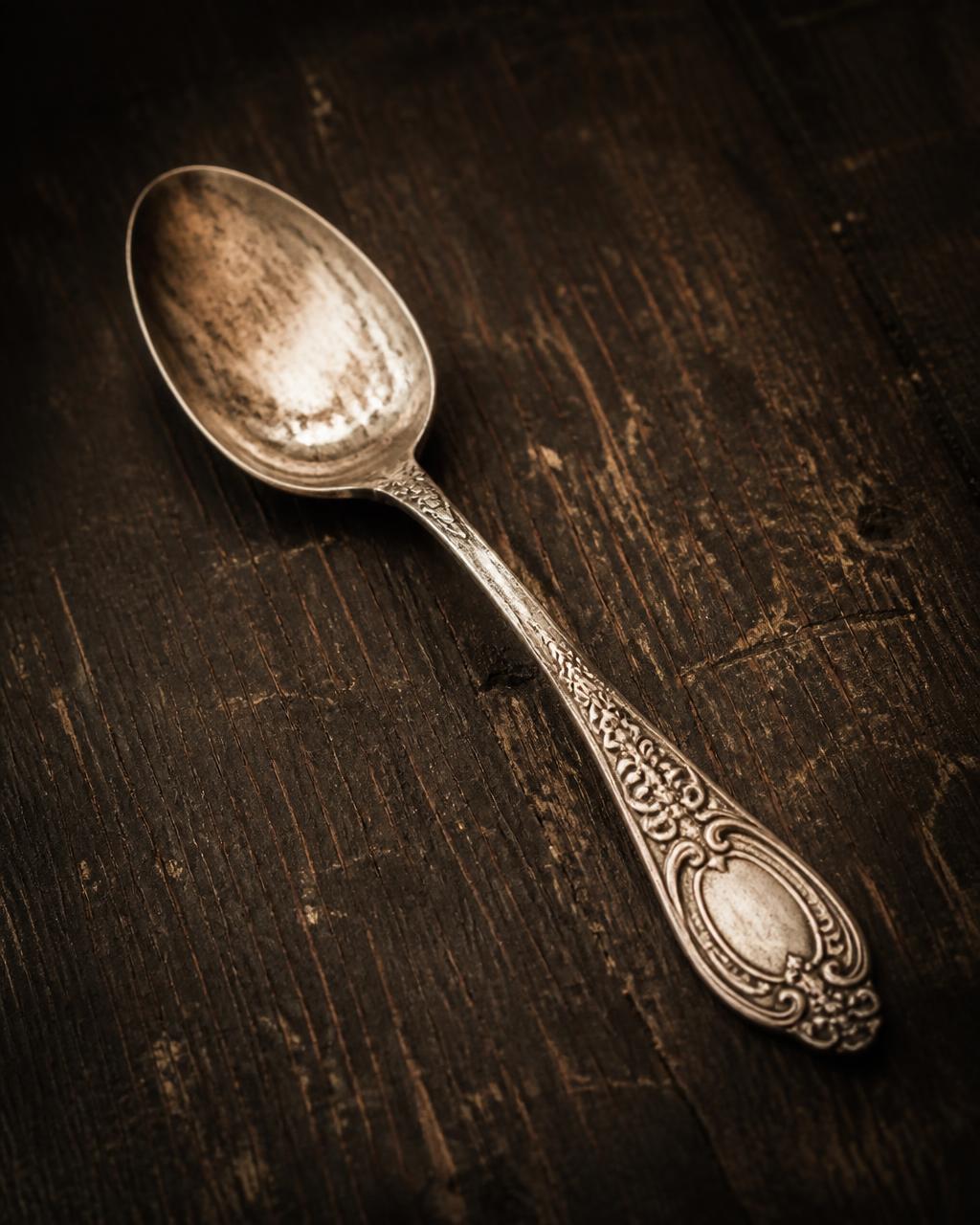 A single ornate vintage silver spoon on dark aged wood